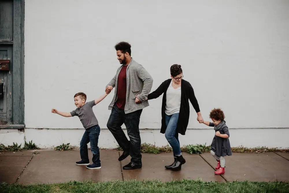 A family of four holding hands and walking along a sidewalk