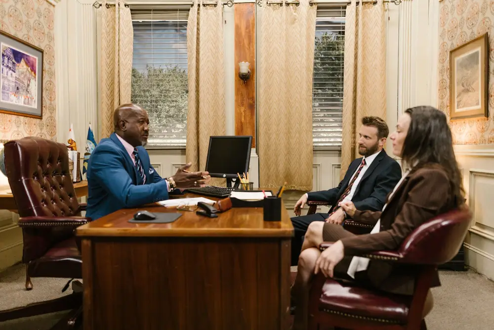 A lawyer in a suit talking with two clients across a desk in an office
